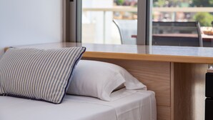 A modern room with a wooden desk, a cushioned bench, and a large window offering a view of buildings and greenery.