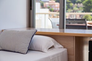A modern room with a wooden desk, a cushioned bench, and a large window offering a view of buildings and greenery.