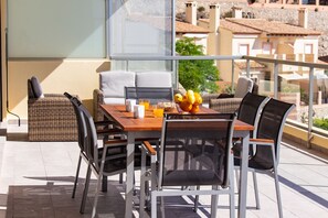A balcony with a wooden table, wicker chairs, and a bowl of fruit. - Sea View Terrace Apartment Cullera (Cullera)
