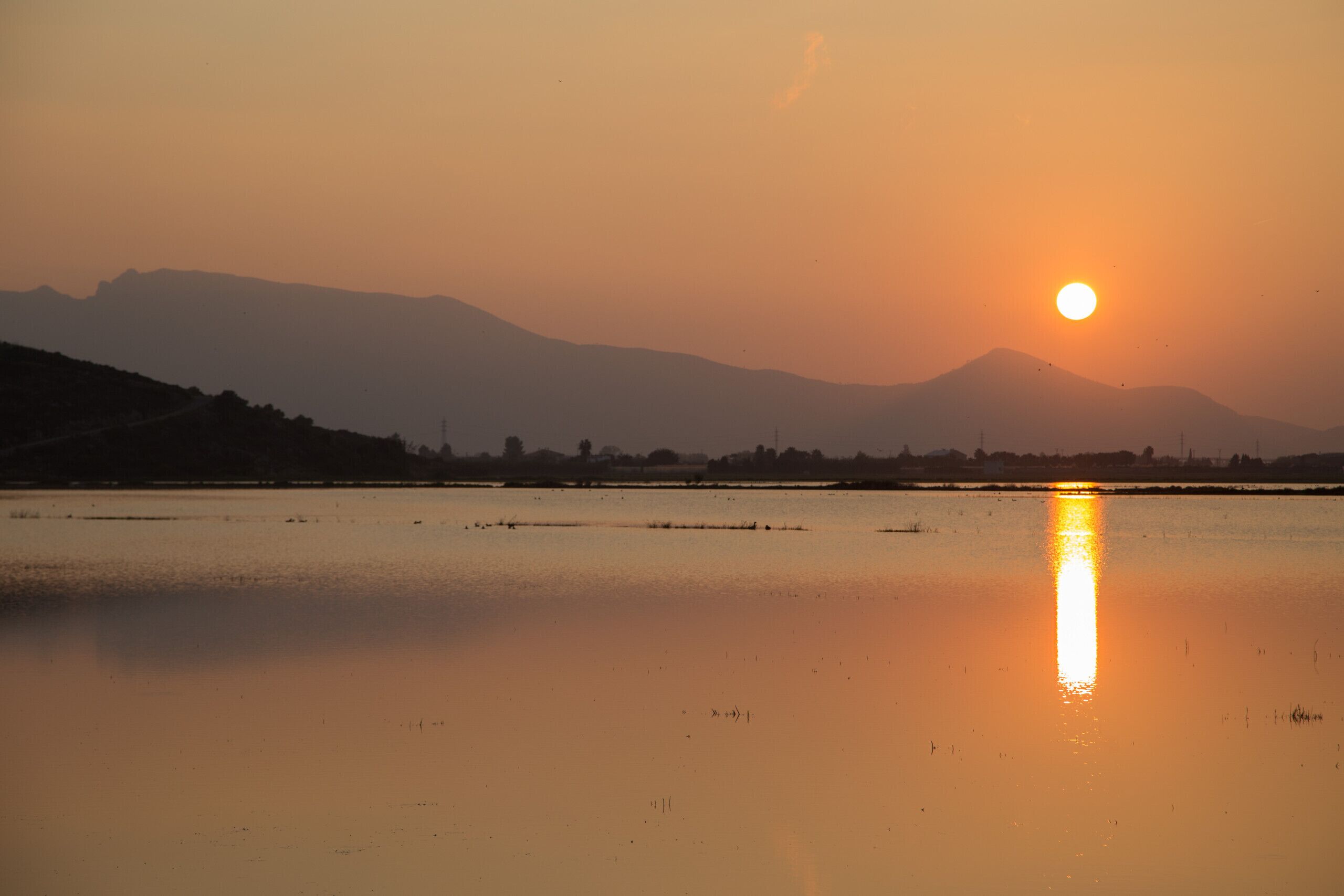 A sunset over a calm body of water with distant mountains.