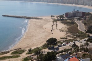 Et hotel ved stranden med udsigt over havet, en parkeringsplads og en vej ned til stranden.