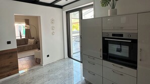 Cocina moderna con armarios blancos, horno empotrado y puerta corrediza de vidrio que da a un patio.