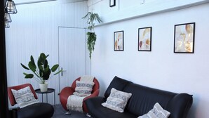Una sala de estar moderna con un sofá de cuero negro, un sillón rojo y una planta en maceta. Hay tres cuadros abstractos enmarcados en la pared.