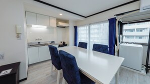 Une cuisine moderne avec des meubles blancs, une cuisinière et un évier. On y trouve également un coin repas avec une table blanche et des chaises bleues.