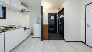 Un couloir étroit, avec une cuisine d’un côté, une porte avec une pancarte et un petit réfrigérateur.