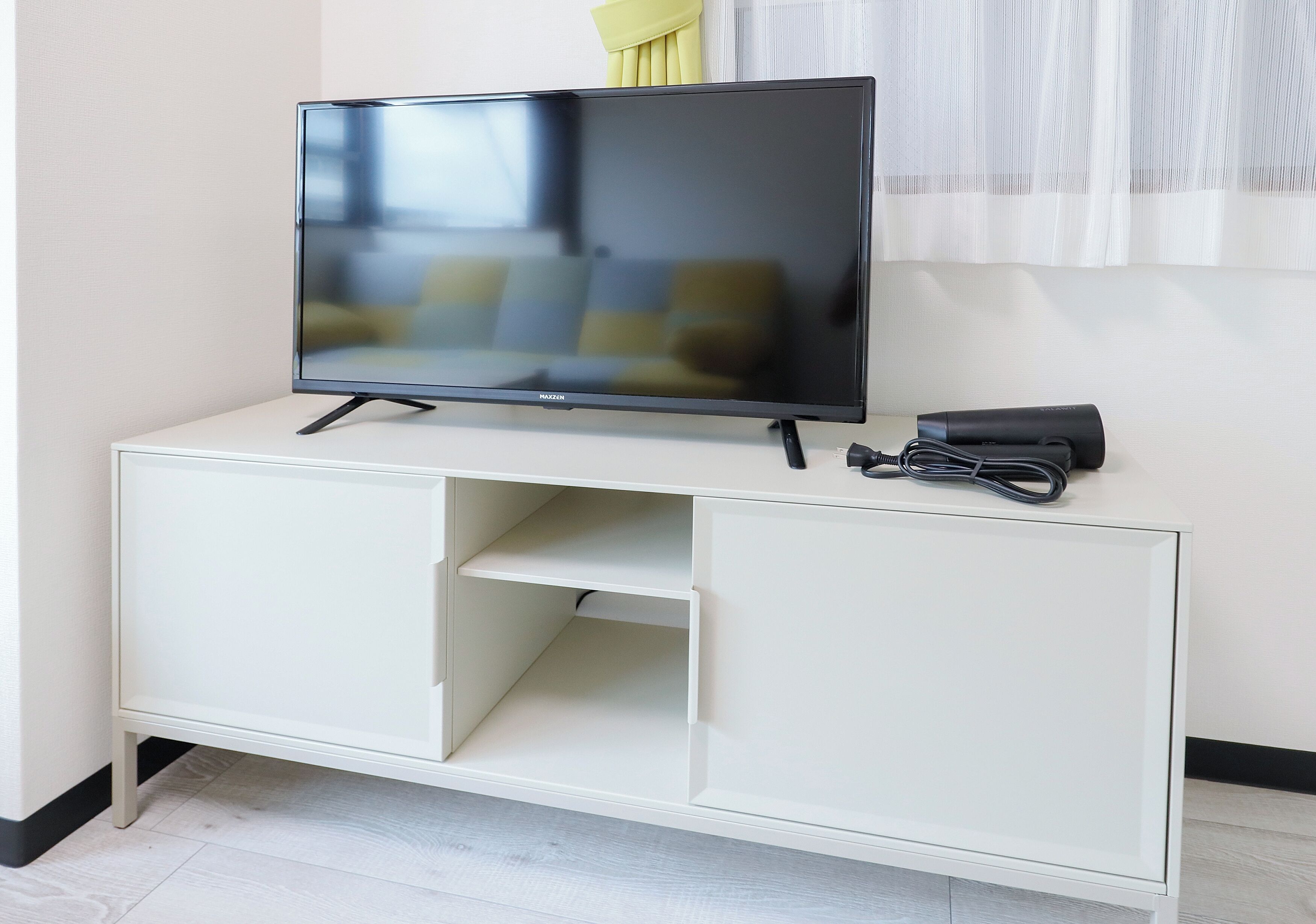 A flat-screen TV on a white cabinet with a remote and cable.