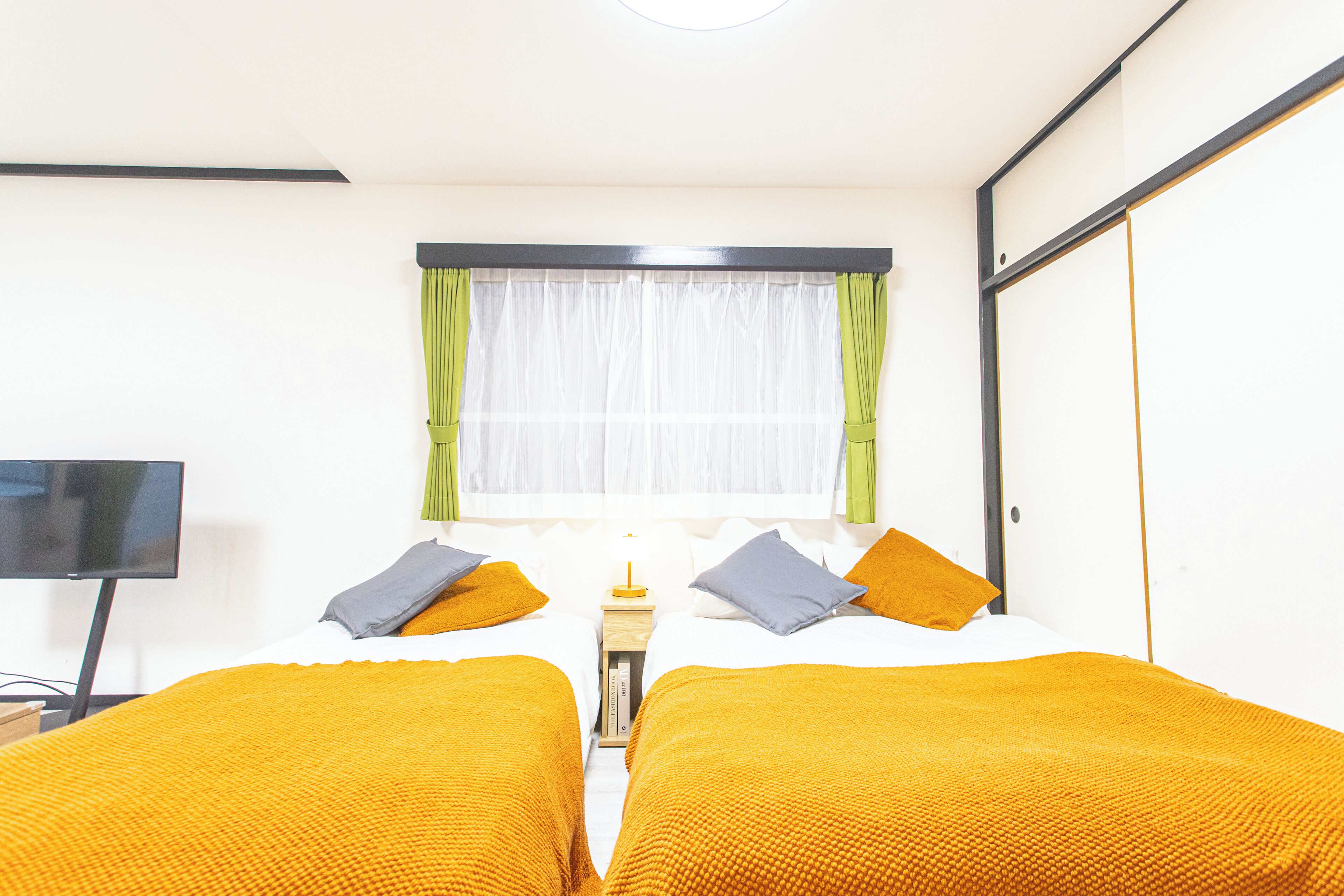 A hotel room with two beds, a television, a window with curtains, and a bedside table.