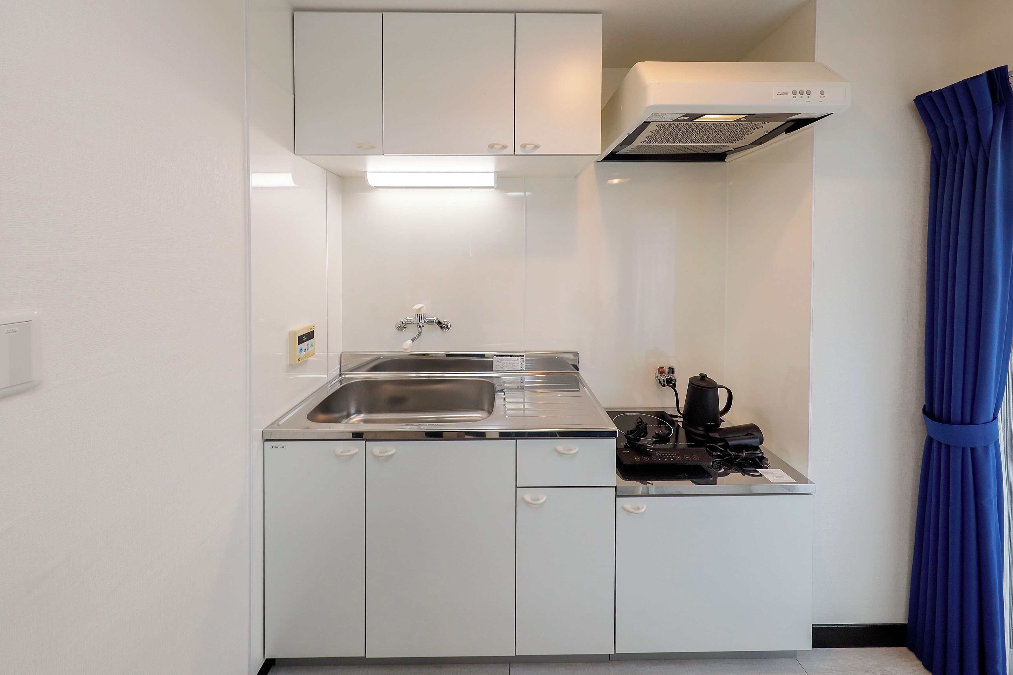 Una kitchenette compacta con un lavamanos de acero inoxidable, estufa y horno empotrado.
