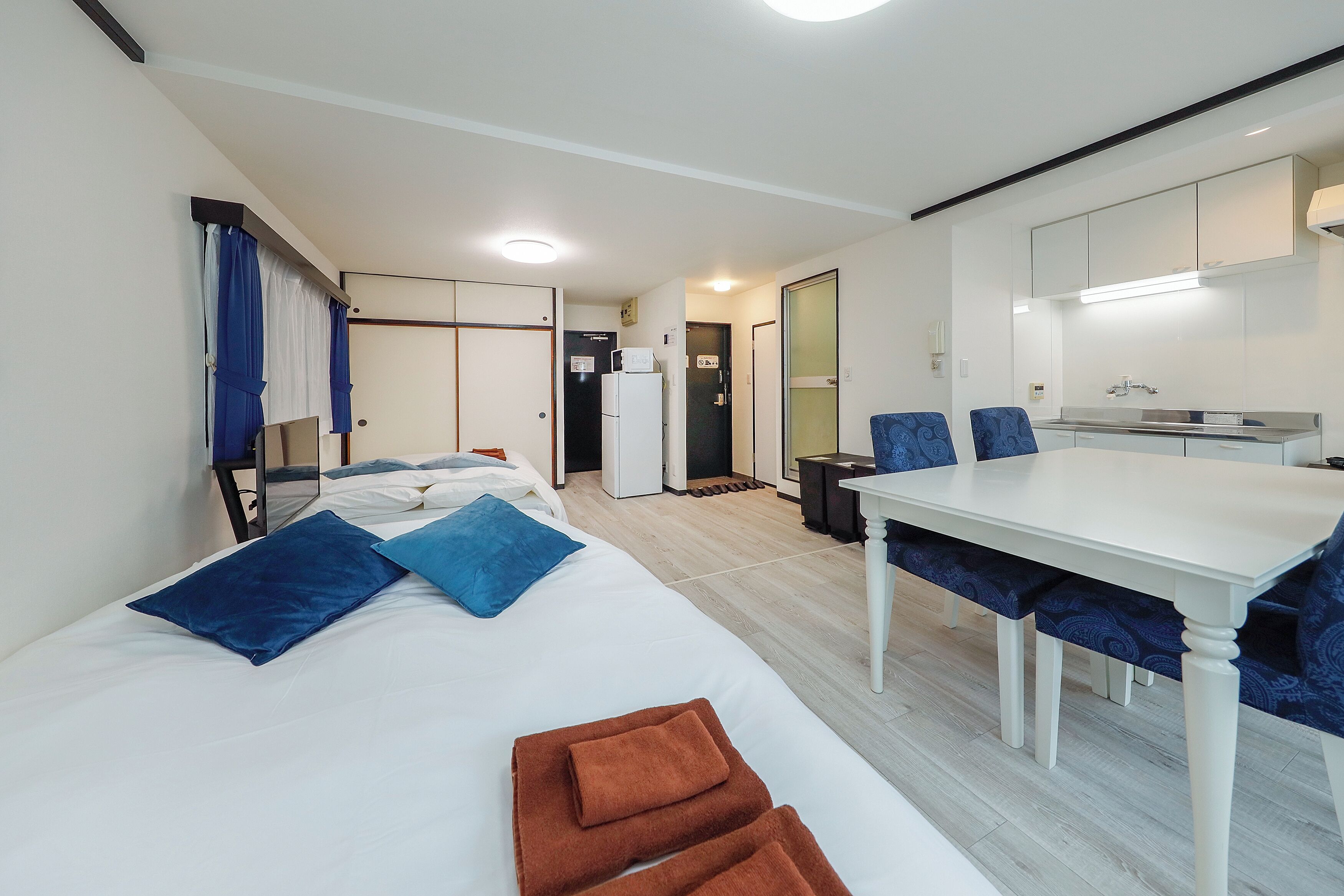 A modern hotel room with a bed, a dining table, and a kitchenette.