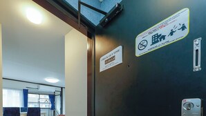 L’entrée d’une chambre d’hôtel, avec un panneau indiquant l’heure limite pour quitter la chambre, un porte-chaussures et une porte dotée d’une serrure et d’un panneau indiquant qu’il est interdit de fumer.