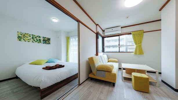 Une chambre moderne avec un lit, un canapé, une petite table et une fenêtre avec des rideaux.