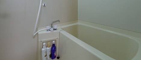 A bathroom with a bathtub, a showerhead, and a hand dryer.