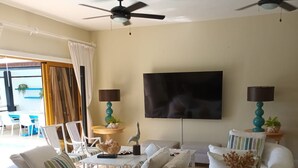 Un salon comprenant un canapé, un téléviseur, un ventilateur de plafond et un coin repas avec une table.