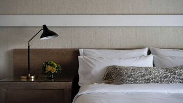 A neatly made bed with white linens and a decorative pillow, a bedside table with a black lamp, and a small vase with yellow flowers.