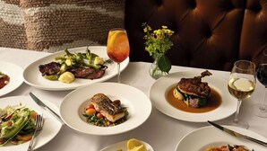 A dining table with various dishes, including steak, fish, and seafood, accompanied by drinks and a vase of flowers. - Seven Beach Lane (Westhampton Beach)