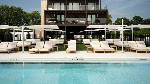 A modern two-story building with a pool area featuring sun loungers and umbrellas. - Seven Beach Lane (Westhampton Beach)