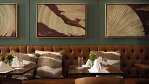 A restaurant with a brown leather booth seating area, tables with white napkins, and framed artwork on the wall. - Seven Beach Lane (Westhampton Beach)