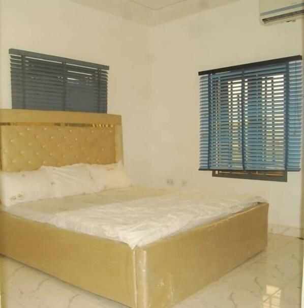 A bedroom with a bed, a headboard, and a window with blinds.