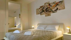 Ein Hotelzimmer mit einem Bett, zwei Nachttischlampen, einem Wandbild im abstrakten Stil und einem Spiegel.