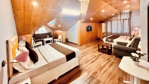 A spacious loft bedroom with a sloped ceiling, wooden flooring, a large bed, a sofa, a TV, and a dining area. - Hotel Hadimba palace  (Manali)