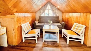 A cozy attic room with wooden walls and a sloped ceiling. There is a sofa, two chairs, and a small table with a vase. - Hotel Hadimba palace  (Manali)