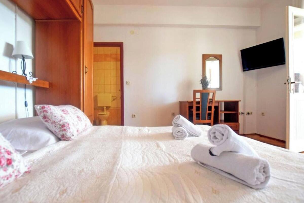 A hotel room with a bed, a desk, a chair, a TV, and a bathroom visible through an open door.