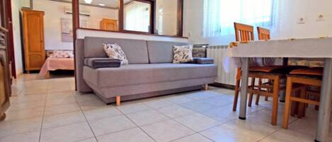A modern living room with a grey sofa, a dining table with chairs, and a kitchen area in the background.