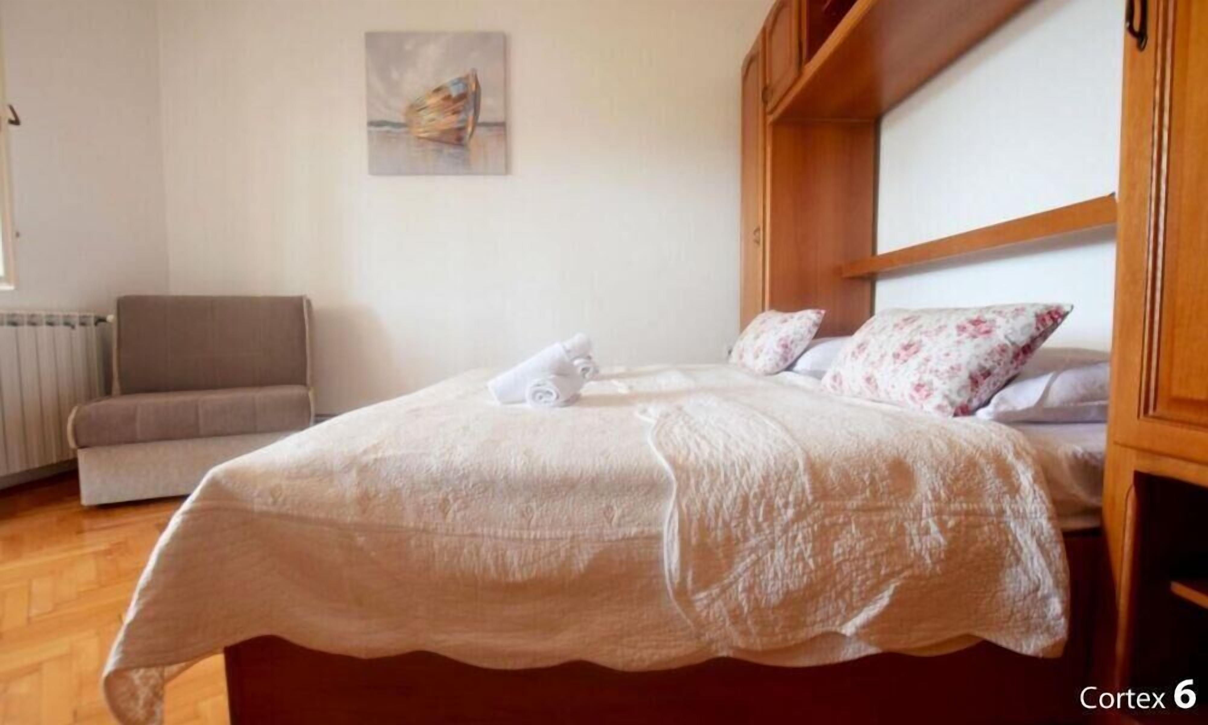 Een opgemaakt bed met een witte dekbedovertrek, een grijze bank en een houten hoofdbord.