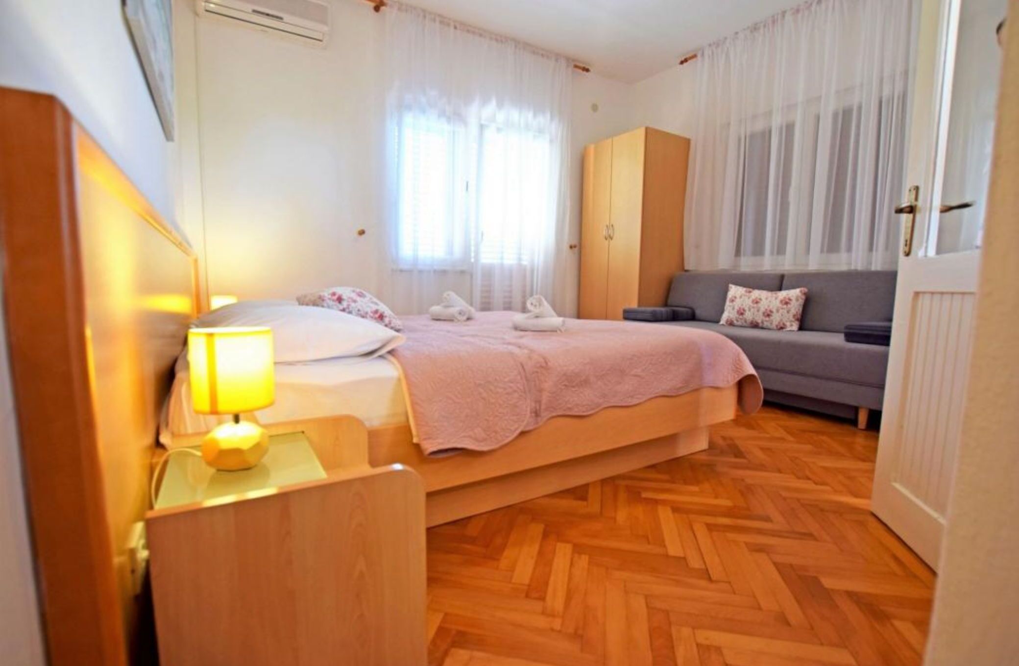 A bedroom with a bed, bedside table, lamp, wardrobe, and a sofa.