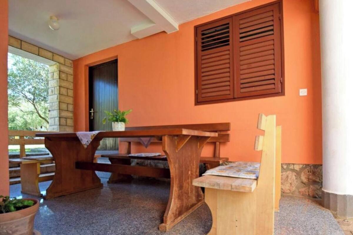 A wooden table and bench set in a covered outdoor area with a stone wall and orange walls.