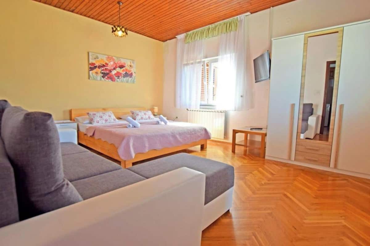 A bedroom with a bed, a sofa, a painting, a TV, and a wardrobe.