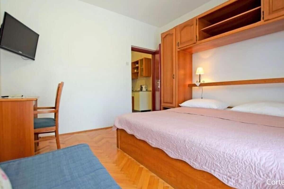 A bedroom with a bed, a desk, a chair, a television, and wooden cabinets.