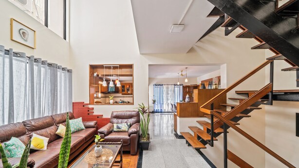 A modern living room with a leather sofa, a coffee table, and a staircase. - 🌳 Namma Woodland Villa | Golf Course Views (Bengaluru)