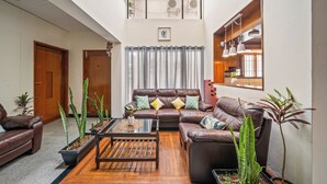 A spacious living room with a brown leather sofa, a wooden coffee table, and potted plants. - 🌳 Namma Woodland Villa | Golf Course Views (Bengaluru)