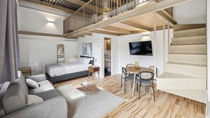 Une chambre d’hôtel moderne avec un espace nuit en mezzanine, une table à manger et un escalier.