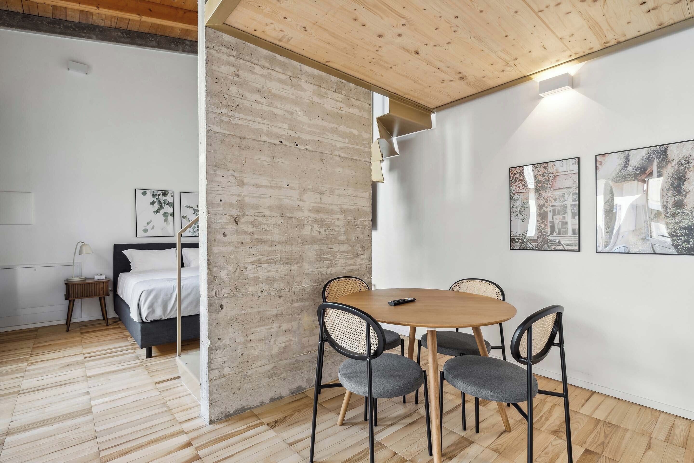 A modern room with a wooden floor, a bed, a dining table with chairs, and artwork on the walls.