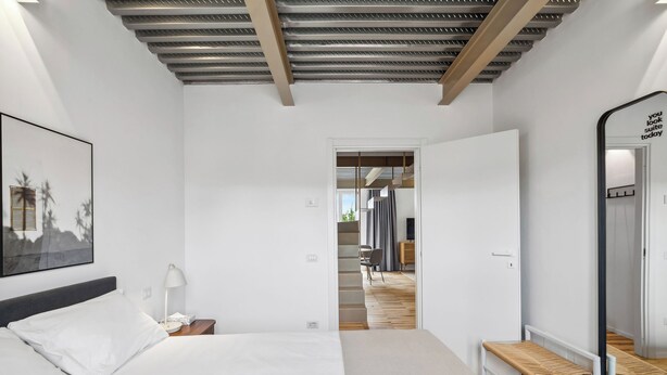 A modern hotel room with a large bed, a bedside table, a lamp, and a mirror.