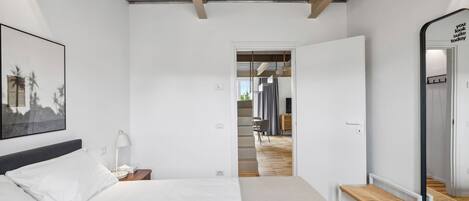 A modern hotel room with a large bed, a bedside table, a lamp, and a mirror.