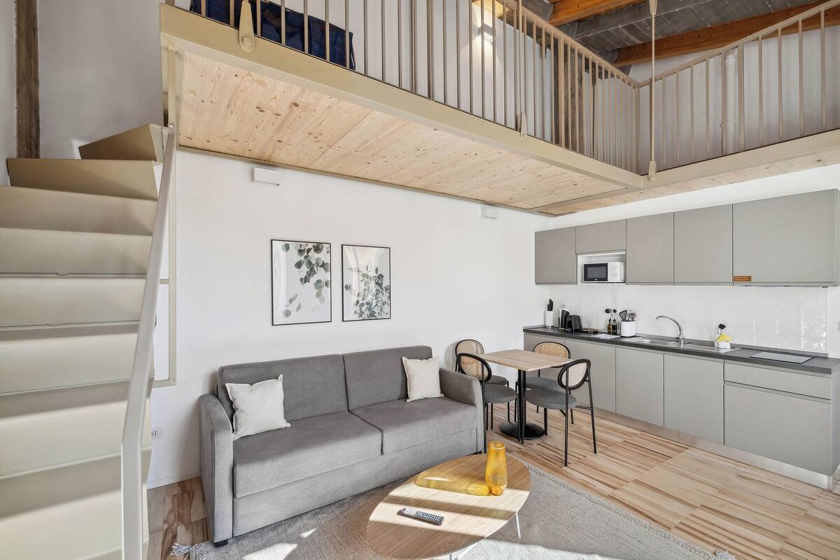 A modern interior with a grey sofa, wooden coffee table, and a staircase leading to a loft area.