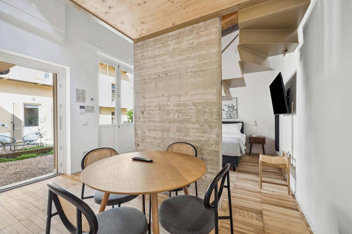 A modern room with a wooden dining table, grey chairs, a staircase, and a TV mounted on the wall.