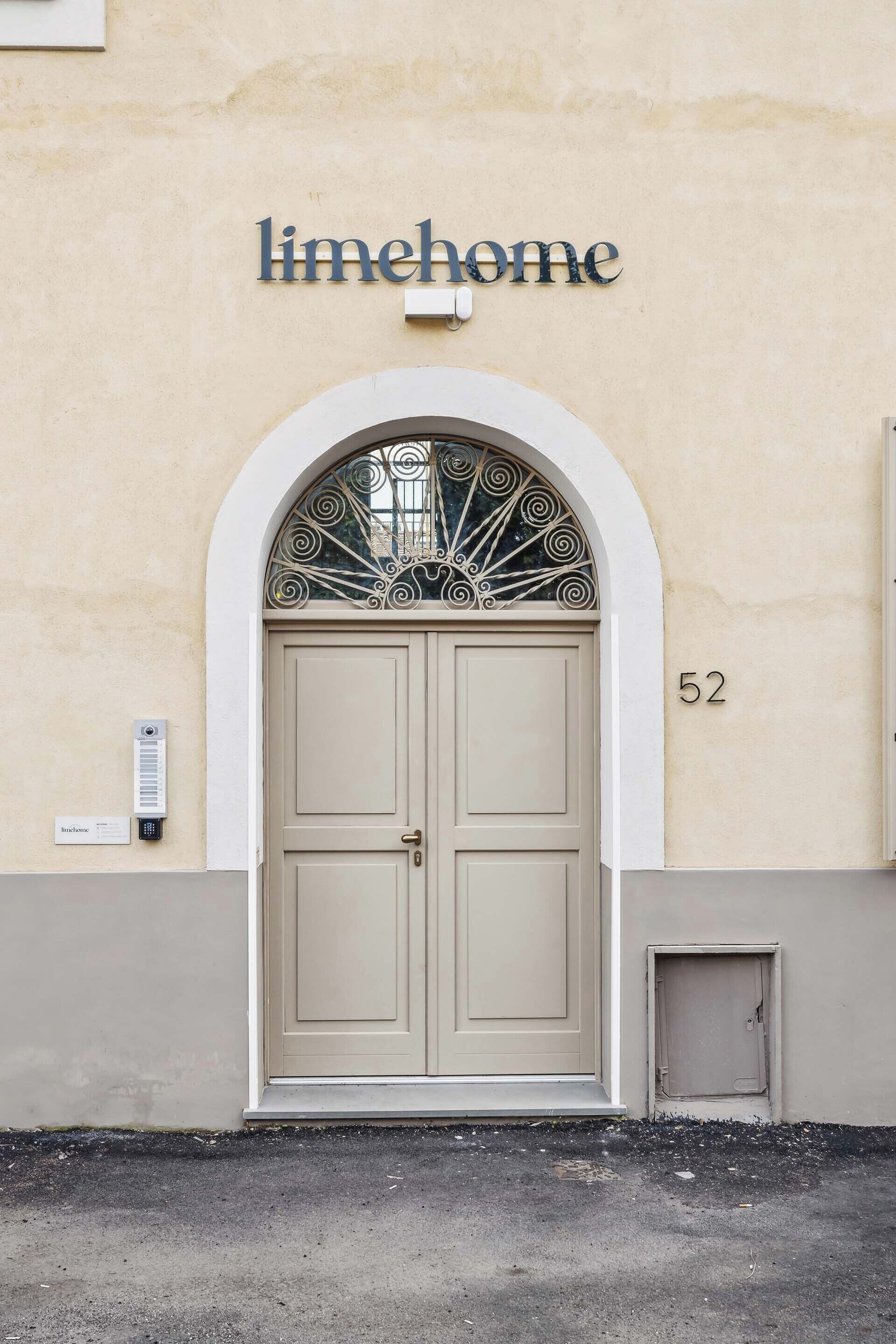 A building with a beige facade, a double door with a decorative metal arch above it, and the name "limehome" displayed above.
