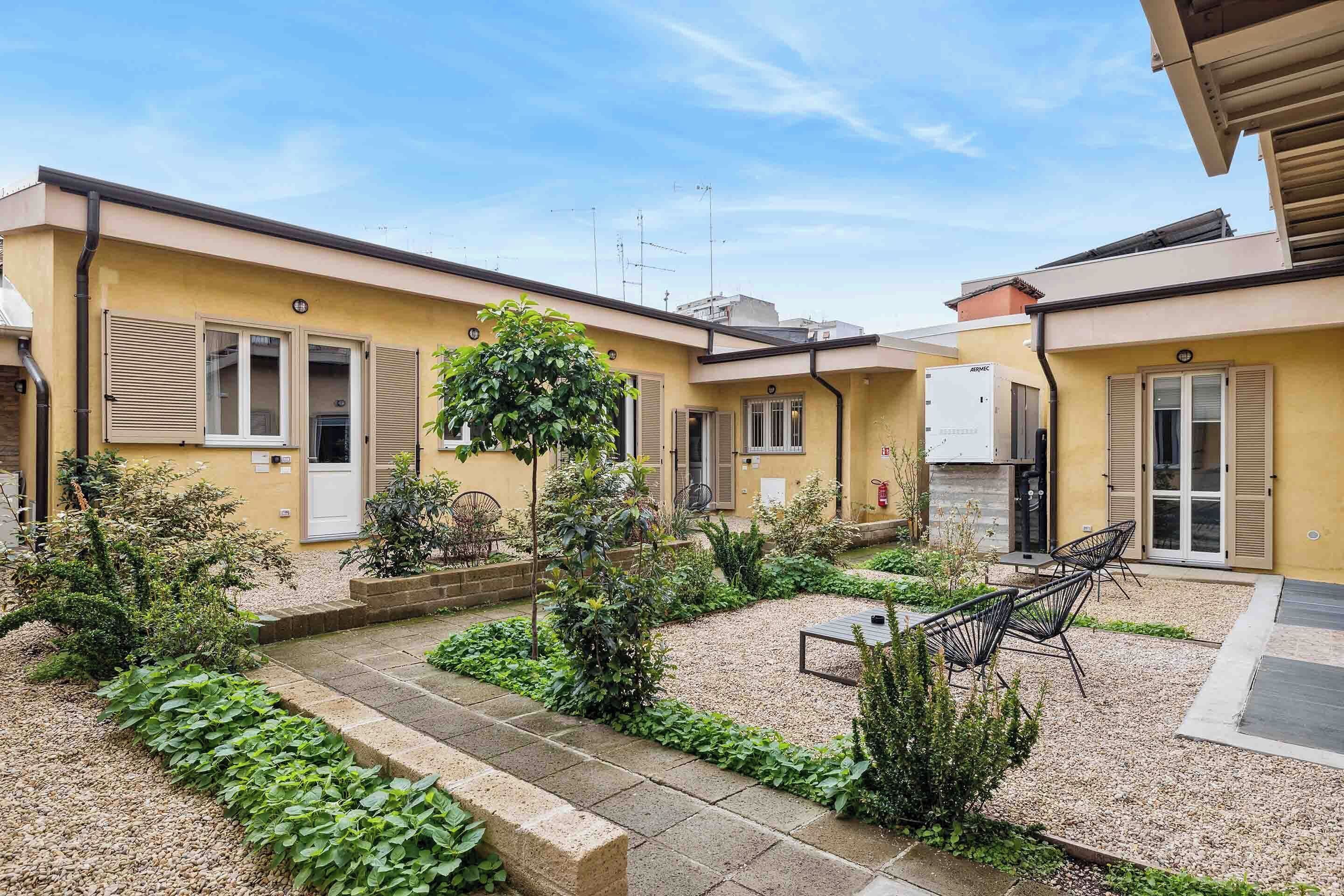 A courtyard with a gravel path, potted plants, and outdoor furniture.