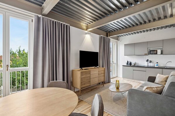 A modern living room with a flat-screen TV, grey sofa, and a dining table. - Limehome Rome Via Fortebraccio (Rome)