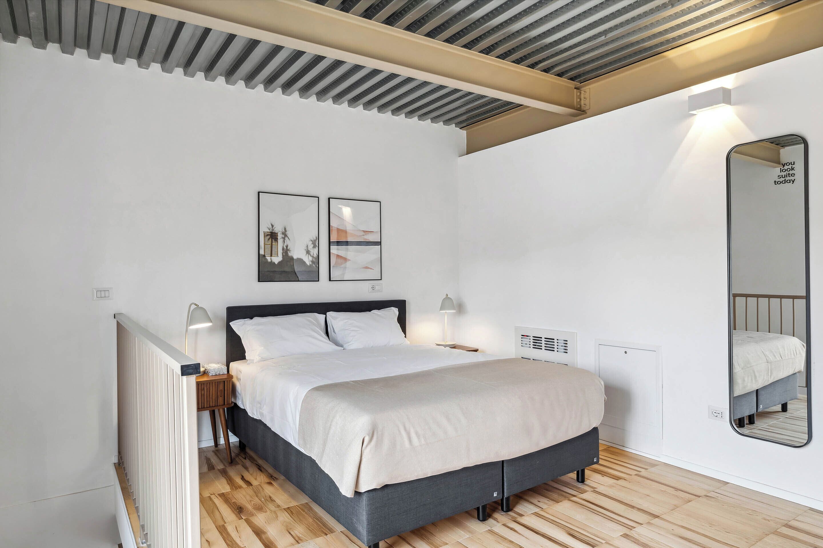 A modern bedroom with a bed, bedside tables, a mirror, and artwork on the wall.