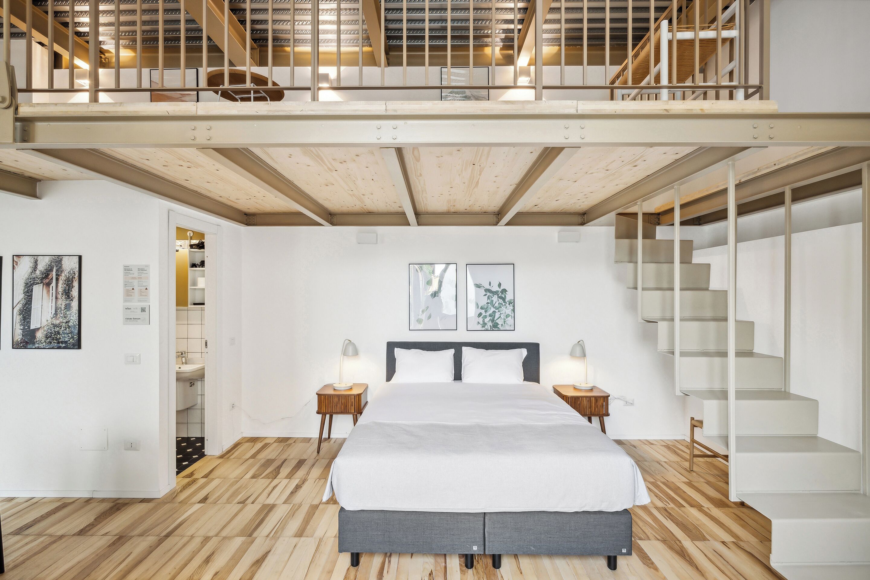 Un dormitorio moderno con una cama grande, suelo de madera, una escalera y una zona en alto.