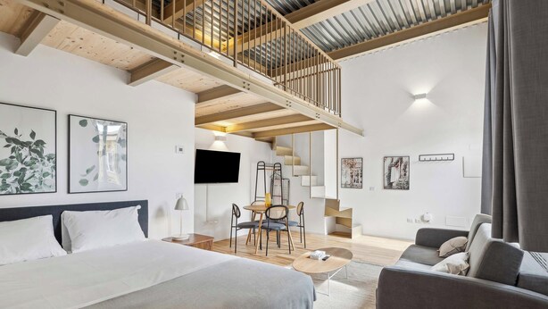 Une chambre d’hôtel moderne dotée d’un grand lit, d’un canapé, d’un coin repas et d’un escalier menant à un niveau supérieur.