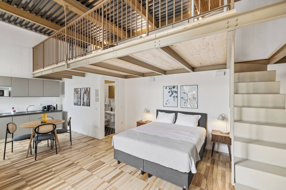 A modern bedroom with a bed, bedside tables, and a staircase leading to an upper level.