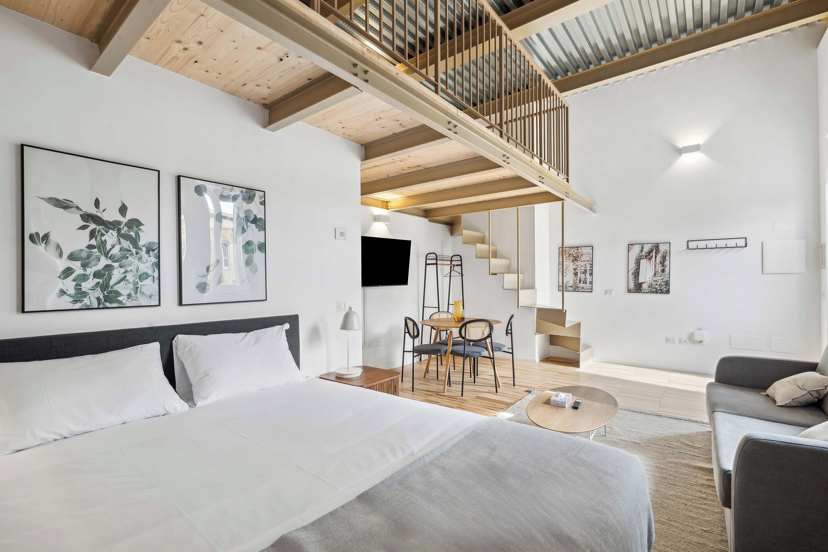 A modern hotel room with a large bed, a dining area, and a staircase leading to an upper level.