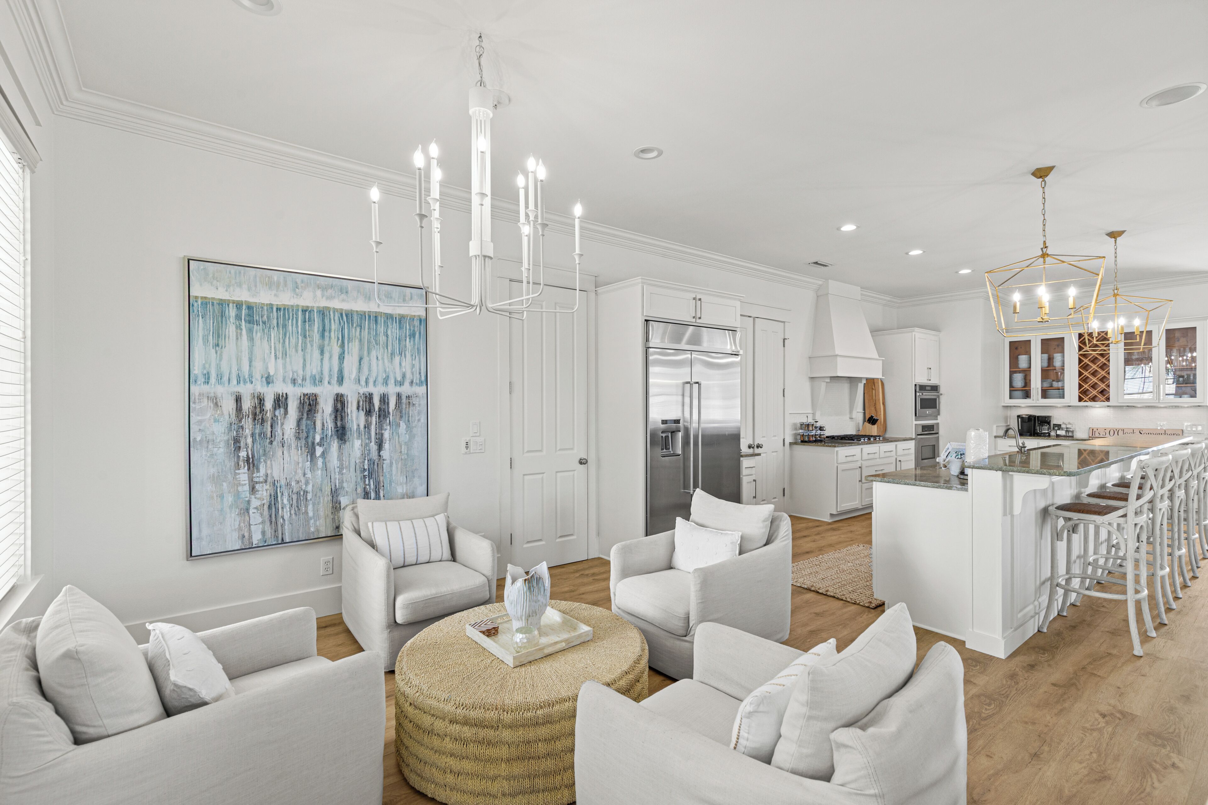 A modern kitchen with a stainless steel refrigerator, white cabinetry, and a bar area with stools.