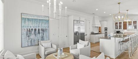 A modern kitchen with a stainless steel refrigerator, white cabinetry, and a bar area with stools.